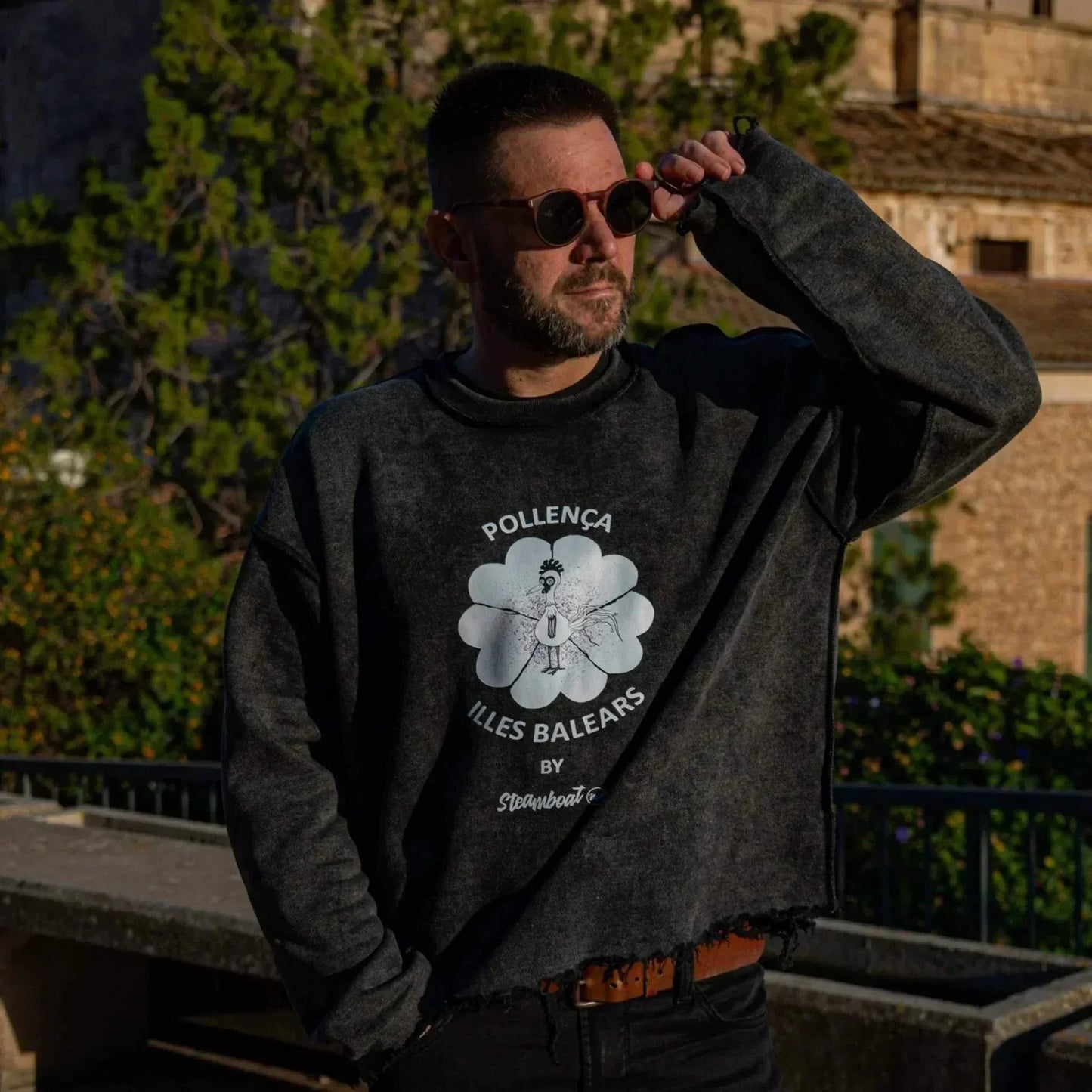 Sudadera Pollença Cropped negro lavado unisex con logo artístico y bordes deshilachados, estilo urbano mediterráneo.