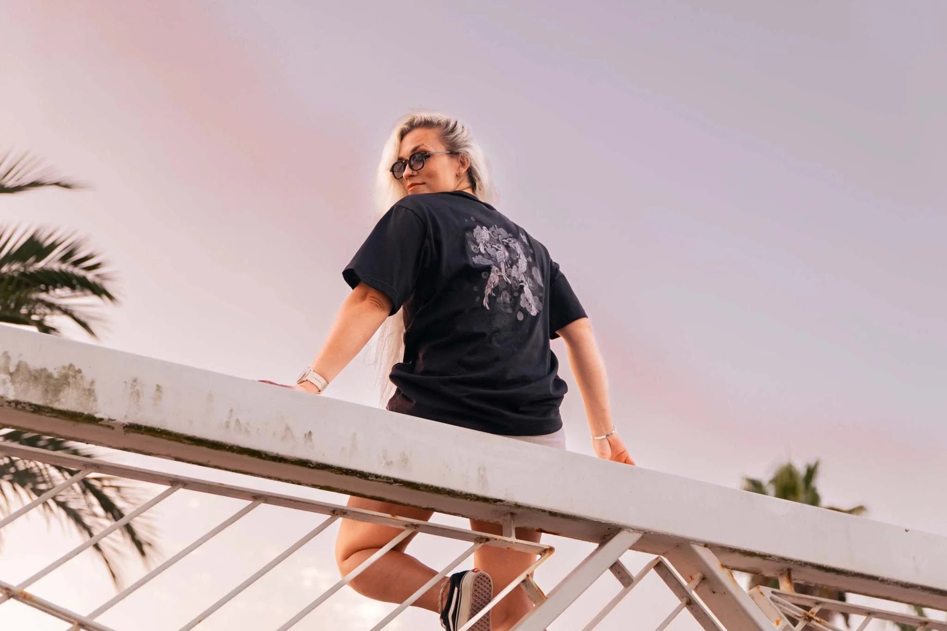 Persona con camiseta Cuervos Nocturnos negra con diseño gótico y estampado oscuro vista desde atrás en exterior al atardecer